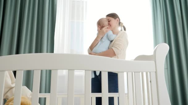 Χαμογελώντας μωρό και μητέρα αγκαλιάζονται στην κρεβατοκάμαρα με μεγάλο παράθυρο το πρωί. Έννοια της γονικής μέριμνας, οικογενειακή ευτυχία και ανάπτυξη του μωρού — Αρχείο Βίντεο