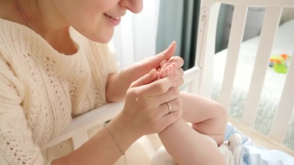 Primo piano di sorridente madre amorevole baciare i piccoli piedi del bambino a letto al mattino. Concetto di genitorialità, felicità familiare e sviluppo del bambino. — Video Stock