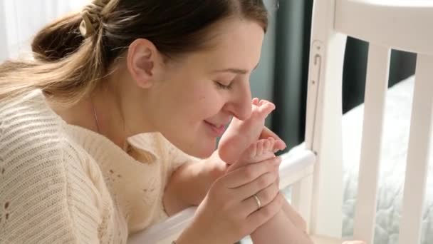 Mamma felice che guarda il suo piccolo figlio a letto e bacia piedini. Concetto di genitorialità, felicità familiare e sviluppo del bambino. — Video Stock