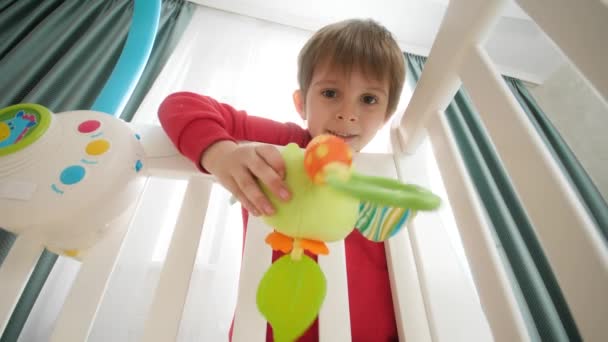 かわいい男の子が弟と遊ぶおもちゃをベビーベッドに寝そべっている。家族の幸せと赤ちゃんの発達の概念. — ストック動画