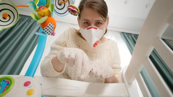 Junge Mutter mit Schutzmaske und Gummihandschuhen spielt mit ihrem Baby im Kinderbett. Konzept der Kindererziehung und Babybetreuung während der Coronavirus-Covid-19-Pandemie. — Stockvideo