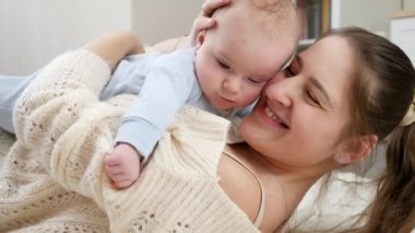 Gülümseyen genç bir annenin portresi yerde yatarken küçük oğlunu kucaklaması ve kucaklaması. Aile mutluluğu ve çocuk gelişimi kavramı