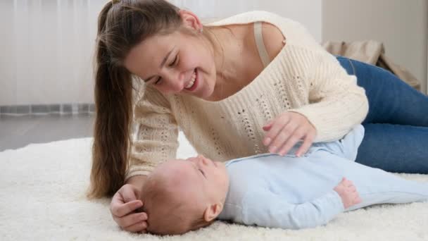 Młoda kochająca matka głaskająca i rozmawiająca ze swoim synkiem leżącym na dywanie w salonie. Pojęcie szczęścia rodzinnego i rozwoju dzieci — Wideo stockowe