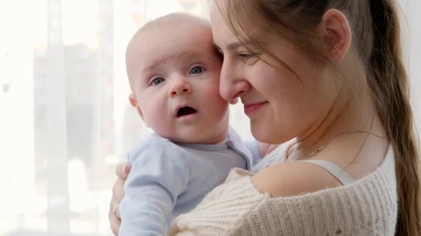 Retrato de primer plano de la cara del bebé y la madre abrazándose y abrazándose en la gran ventana en casa. Concepto de felicidad familiar y desarrollo infantil — Vídeos de Stock