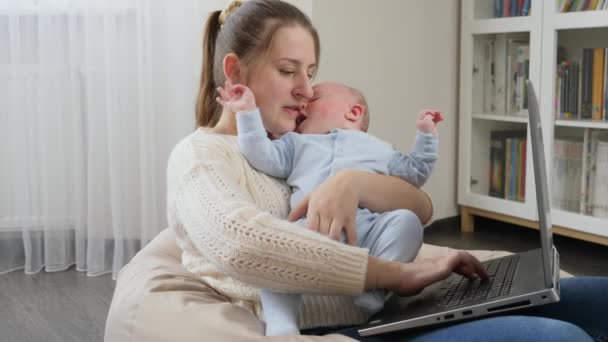 Umtriebige freiberufliche Mutter arbeitet vom Home Office aus am Laptop und hält weinenden kleinen Sohn — Stockvideo