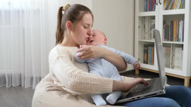 Jonge moeder streelde haar baby terwijl ze thuis werkte op laptop. Begrip gezinsgeluk en ontwikkeling van kinderen — Stockvideo