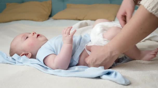Aranyos kisfiú néz anyára, miközben kicseréli a koszos pelenkáját az ágyban. Szülői, babahigiéniai és gyermekfejlődési koncepció — Stock videók