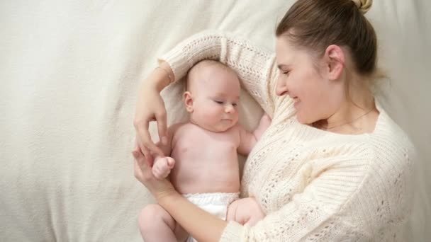 Minik oğluyla birlikte bebek bezi içinde yatan ve onu nazikçe canlandıran şefkatli bir anne. Ebeveynlik kavramı, bebek hijyeni ve çocuk bakımı — Stok video