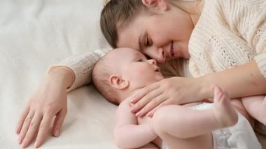 Sevimli küçük oğlan, gülümseyerek annesine dokunuyor. Yatakta yanında yatıyor. Ebeveynlik kavramı, bebek bakımı ve aile mutluluğu.