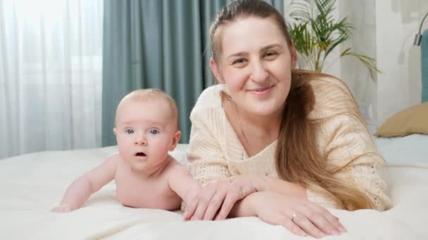 Menino adorável com a mãe deitada na cama e sorrindo para a câmera. Conceito de parentalidade, cuidado do bebê e felicidade familiar — Vídeo de Stock