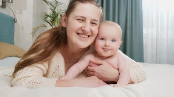 Glimlachend jongetje met gelukkige moeder die in bed ligt en in de camera kijkt. Begrip ouderschap, babyverzorging en gezinsgeluk — Stockvideo