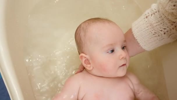 Zbliżenie matki podtrzymującej główkę dziecka podczas mycia w wannie. Pojęcie rodzicielstwa, opieki nad dziećmi i opieki zdrowotnej. — Wideo stockowe
