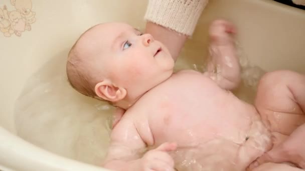 Aranyos baba, ahogy anyát nézi, miközben műanyag fürdőben mossa. A szülői, gyermekgondozási és egészségügyi ellátás fogalma — Stock videók