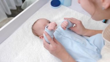Annesi jimnastik yaparken ve tuvalet masasında masaj yaparken tatlı erkek bebek gülümsüyor. Hijyen, bebek bakımı ve sağlık hizmetleri kavramı