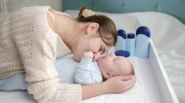 Gülümseyen anne yatak odasındaki tuvalet masasında uzanan küçük oğluyla oynuyordu. Hijyen, bebek bakımı ve sağlık hizmetleri kavramı