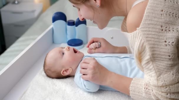 Tersenyum ibu muda tersenyum dan berbicara dengan bayi laki-lakinya berbaring di meja rias. Konsep kebersihan, perawatan bayi dan perawatan kesehatan — Stok Video