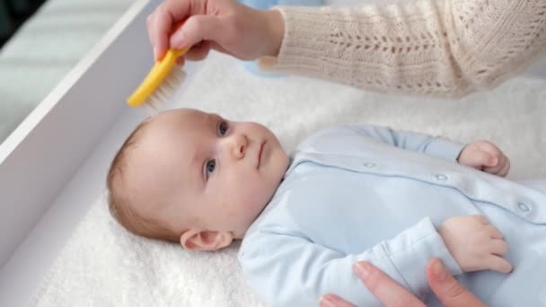 CLoseup de jeune mère peignant ses cheveux de bébé fils avec une brosse à cheveux. Concept d'hygiène, de soins pour bébés et de santé — Video