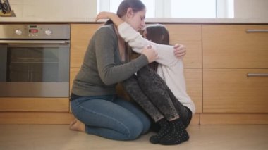 Mutfak zemininde oturmuş annesini kucaklayan üzgün bir genç kız. Gençlerin zihinsel sorunları ve depresyonu