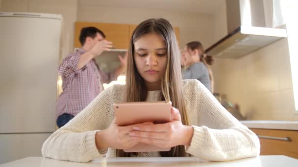 Egy fiatal lány táblagépet használ, és figyelmen kívül hagyja a veszekedő és kiabáló szülőket. Családi erőszak, konfliktusok és kapcsolati problémák — Stock videók