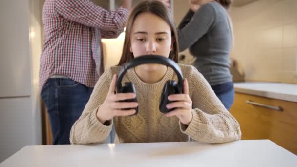 Adolescente fermant les oreilles avec des écouteurs pendant que les parents se disputent, crient et crient en arrière-plan. Violence familiale, conflits et problèmes relationnels — Video