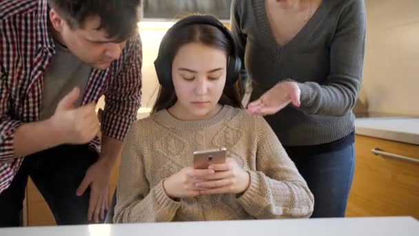 Девочка-подросток слушает музыку и пользуется смартфоном, пока родители кричат и спорят с ней. Семейное насилие, конфликты и проблемы в отношениях — стоковое видео