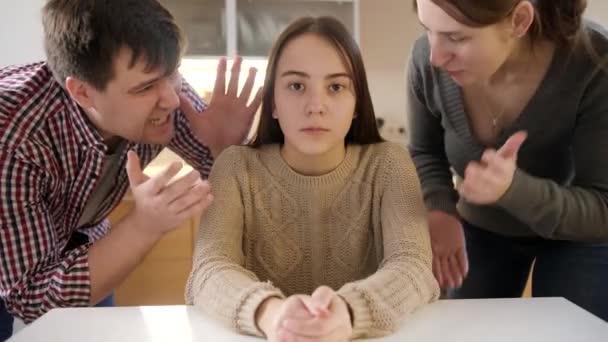 Padre y madre gritando y gritando a la hija adolescente sentada detrás de la mesa en la cocina. Violencia familiar, conflictos y problemas de relación — Vídeo de stock