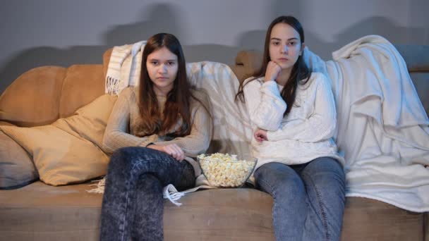 Duas adolescentes assistindo TV no sofá e comendo pipocas à noite — Vídeo de Stock