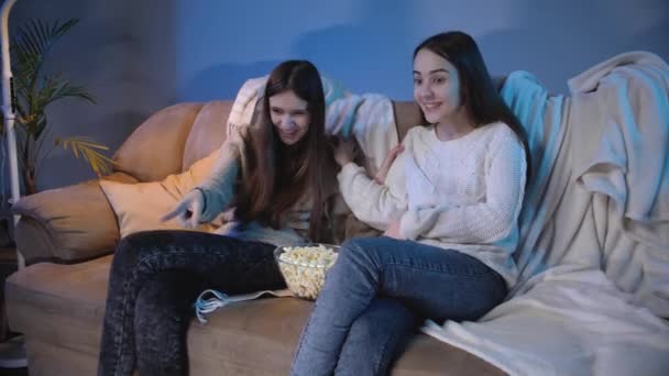 Dwie śmiejące się dziewczyny bawiące się podczas oglądania komedii lub zabawnego wideo w telewizji w nocy — Wideo stockowe