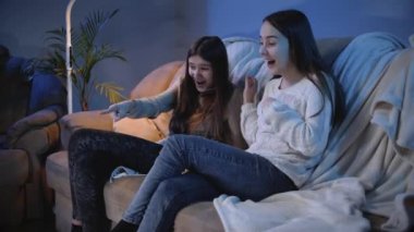 İki gülümseyen kız gece televizyonda komik komedi filmlerine gülüp gülüyor.