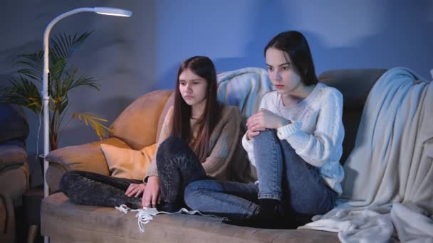 Две девочки-подростки закрывают глаза во время просмотра ужастиков по телевизору ночью — стоковое видео