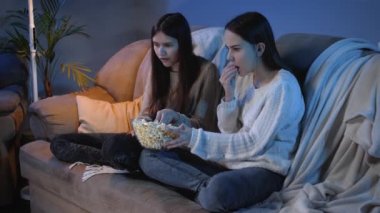 Arkadaşlar büyük kaseden patlamış mısır yerken gece oturma odasında televizyon izliyorlar.
