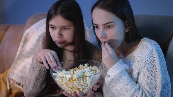 Dvě dívky jíst popcorn z velké misky při sledování horor filmu v televizi — Stock video