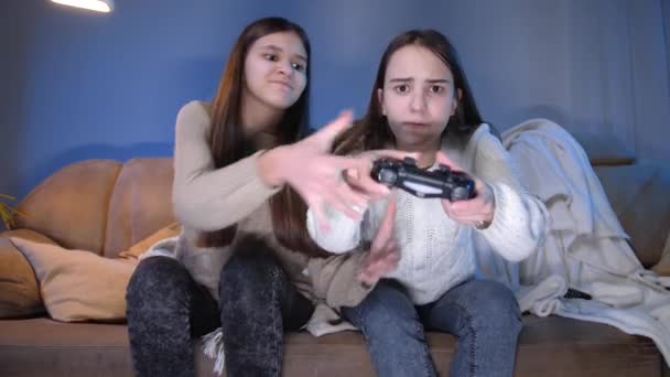 Dos chicas concentradas jugando videojuegos en la consola de juegos en la sala de estar por la noche — Vídeos de Stock