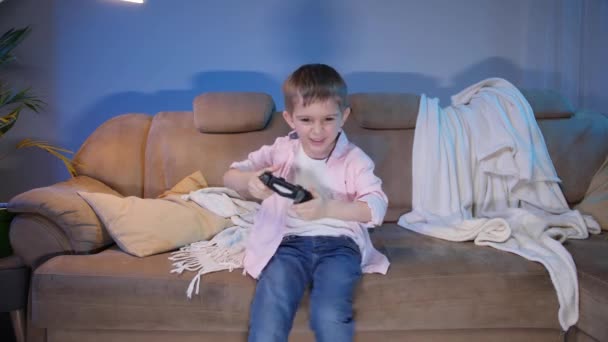 Komik heyecanlı çocuk TV konsolunda geceleri kanepede oyun oynuyor. — Stok video
