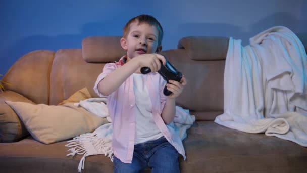 Divertido niño sosteniendo el controlador de juego mientras juega videojuegos en la consola de TV por la noche — Vídeos de Stock