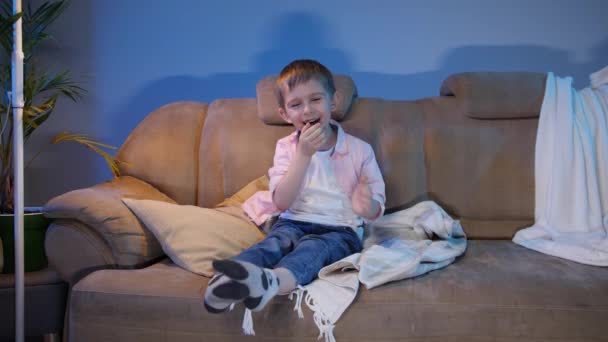 Счастливый маленький мальчик смеется над смешным шоу или комедийным фильмом по ночам — стоковое видео