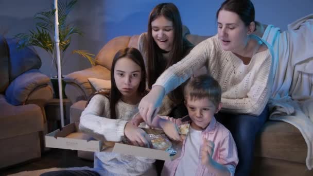 O familie mare mănâncă pizza și ia felii din cutie în timp ce se uită la emisiune TV sau film în camera de zi — Videoclip de stoc