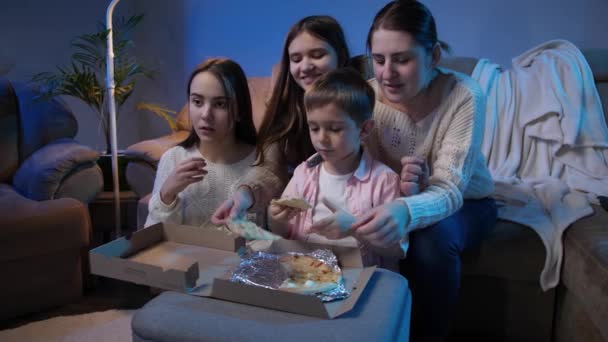 Felice famiglia sorridente godendo mangiare pizza e guardare lo spettacolo televisivo sul divano di notte — Video Stock