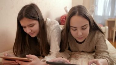Yatakta tablet kullanan iki kız kardeş. Gençler evde modern aletler kullanıyor ve okuyorlar.