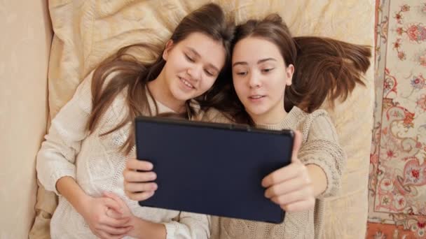 Vista superior de dos niñas acostadas en la cama y el uso de la tableta. Estudio remoto y comunicación desde el hogar — Vídeos de Stock