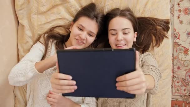 Heureuses adolescentes souriantes se détendre sur le lit et avoir une conversation vidéo en ligne. Etude à distance et communication depuis la maison — Video