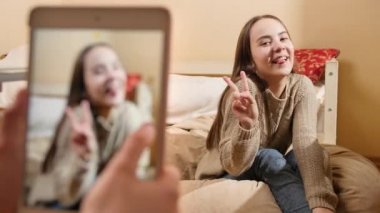 Sosyal medya için akıllı telefondan evde gülümseyen güzel bir genç kızın fotoğraflarını çekmek. Modern iletişim, sosyal medya ve aygıtlar