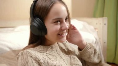 Mutlu gülümseyen kız evde kulaklıkla müzik dinliyor.