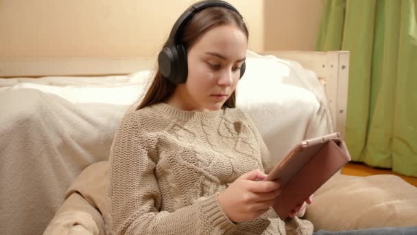Uśmiechnięta nastolatka przeglądająca internet na tablecie i słuchająca muzyki w słuchawkach — Wideo stockowe