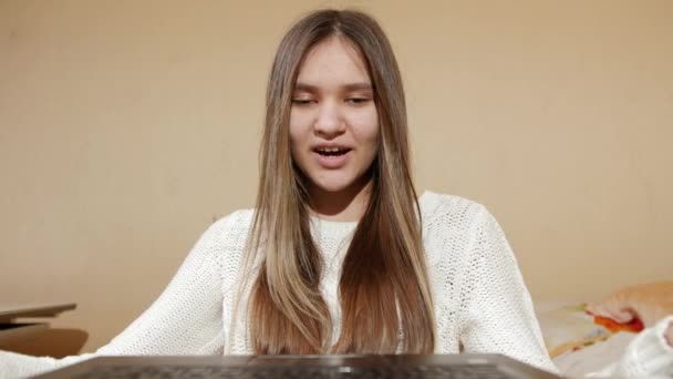Portret van lachend tienermeisje zittend achter laptop en met videoconferentie in haar slaapkamer — Stockvideo