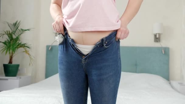 Junge, glückliche Frau gelingt es, enge, kleine Jeans anzuziehen und anzuziehen. Konzept von übermäßigem Gewicht, fettleibigen Frauen, Diät- und Übergewicht-Problemen — Stockvideo