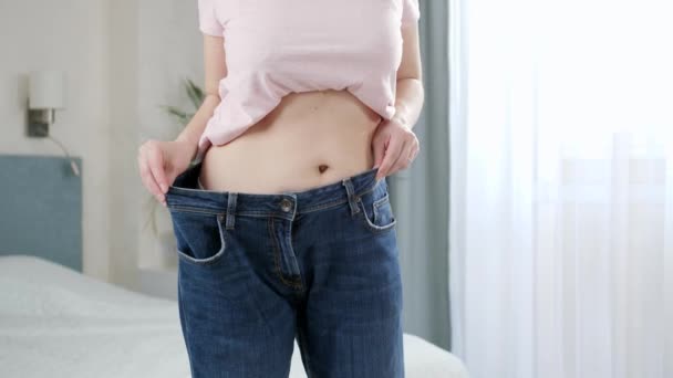 Młoda kobieta z płaskim brzuchem, pozująca w dużych dżinsach. Pojęcie diety, utraty wagi i zdrowego stylu życia. — Wideo stockowe