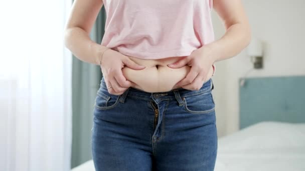 CLoseup de mujer joven en jeans sosteniendo pliegue de grasa en su vientre. Concepto de exceso de peso, obesidad femenina, dieta y problemas de sobrepeso — Vídeos de Stock