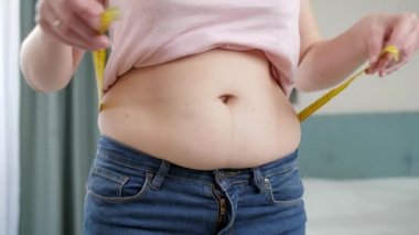 Genç bir kadın, kocaman göbeğini mezurayla ölçüyor. Diyet anlayışı, sağlıksız yaşam tarzı, aşırı kilolu ve obezite