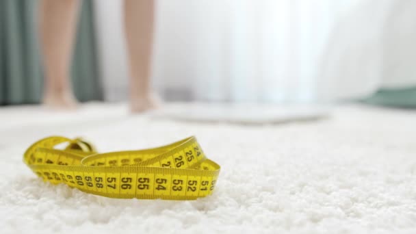 Measuring tape lying on floor next to woman standing on scales in bedroom. Concept of dieting, loosing weight and healthy lifestyle. — Stock Video